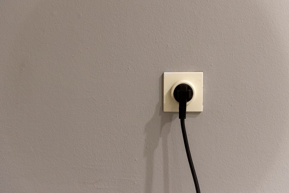 A black mains plug inserted into a white UK wall socket — the type of portable appliance covered by PAT testing