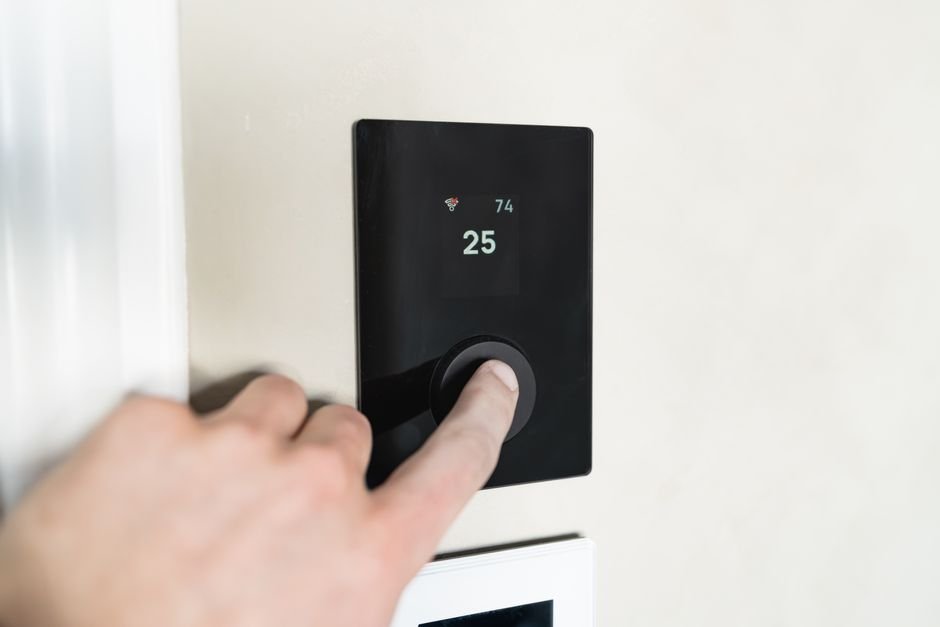 A hand adjusting a modern smart thermostat, the kind of control most new boiler installations are paired with