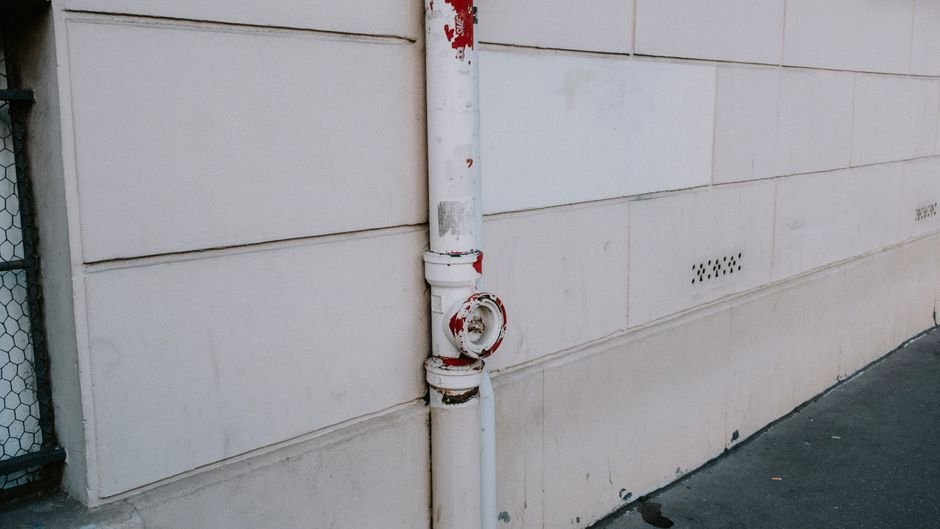 A weathered external drainpipe on a building wall, the kind of corrosion sea air causes on exposed pipework and boiler flues on the coast