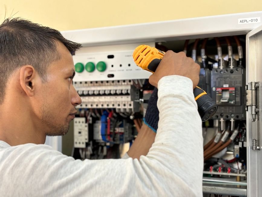 Electrician using a drill on an indoor circuit breaker panel, relevant to EICR and rewiring checks in older flats