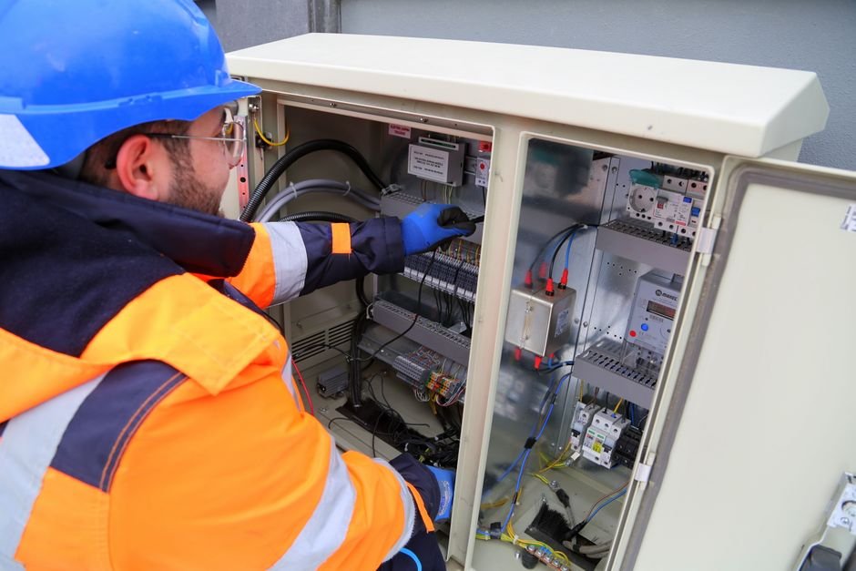 Electrician in safety gear inspecting a fuse box, the kind of consumer unit work Bearsden electricians carry out