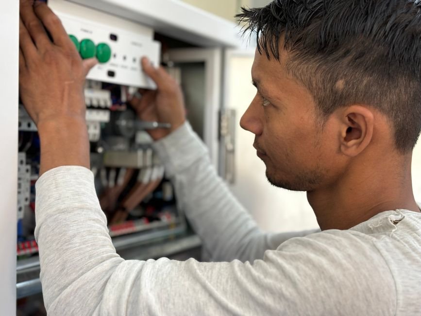 Electrician working inside a domestic electrical panel, checking circuits and connections during a fuse board job