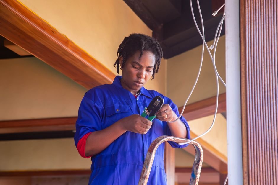 Electrician working from a ladder to wire a ceiling fitting, similar to fitting interlinked smoke alarms in a home