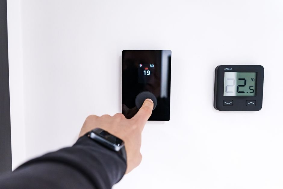 Hand adjusting a digital thermostat, one of the quick checks worth trying before booking an emergency plumber in Giffnock