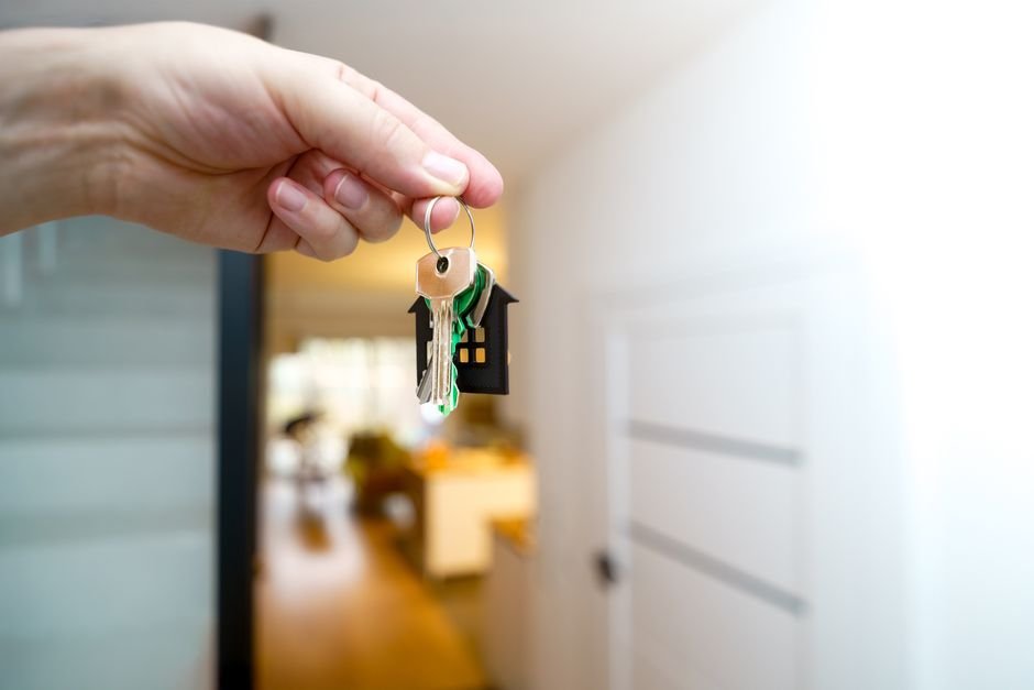 A hand holding a set of house keys inside a rental flat, representing a Scottish landlord's legal responsibilities before letting a property