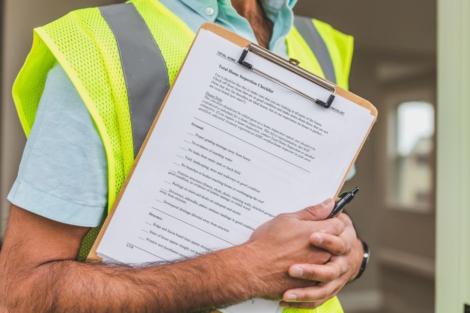A home inspector in a safety vest holding a pen and checklist, representing the safety inspections behind a landlord's legal certificates in Scotland