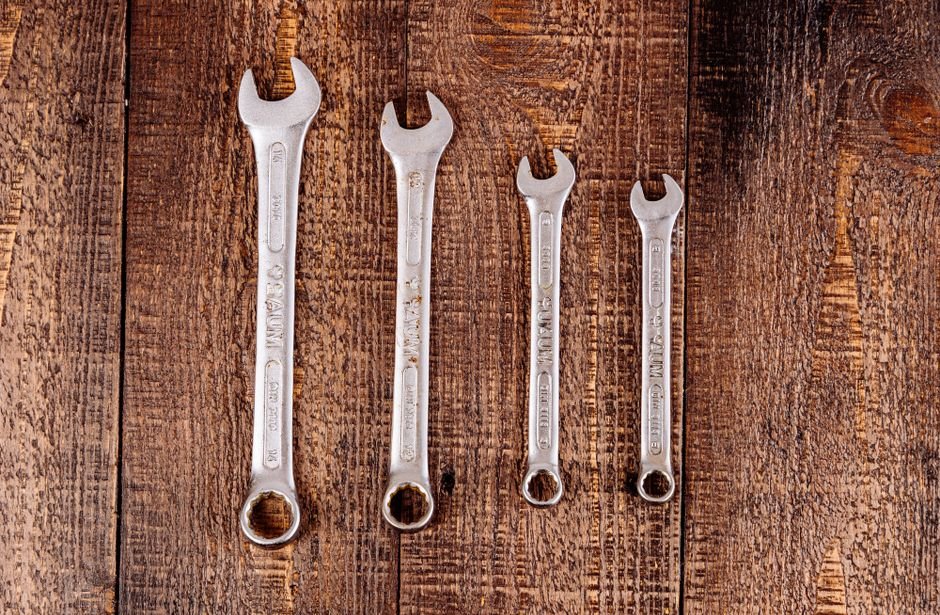 Set of metal plumbing wrenches laid out on a wooden surface, tools used for tenement pipework repairs in Partick