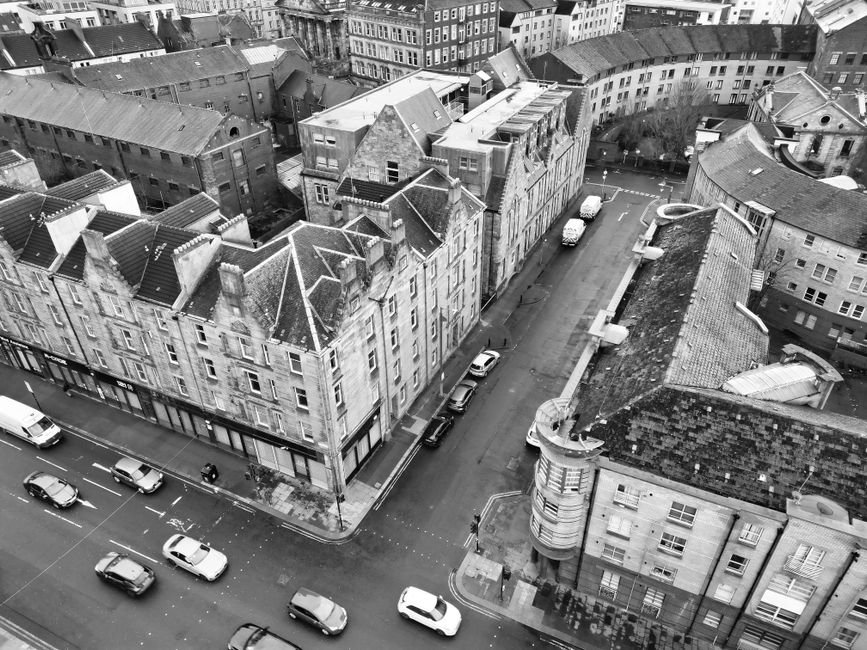 Aerial black-and-white view of red sandstone tenement rooftops and chimney stacks on a Glasgow Southside street, typical of the tenement housing on Pollokshields' east side
